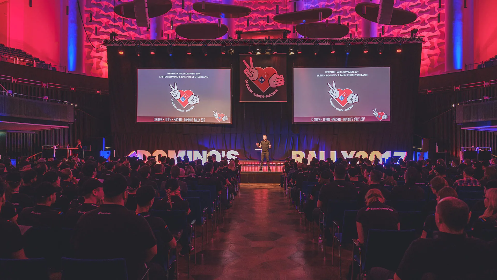 Event host Felix Uhlig on stage at the first Domino's Rally in Germany in front of a full auditorium