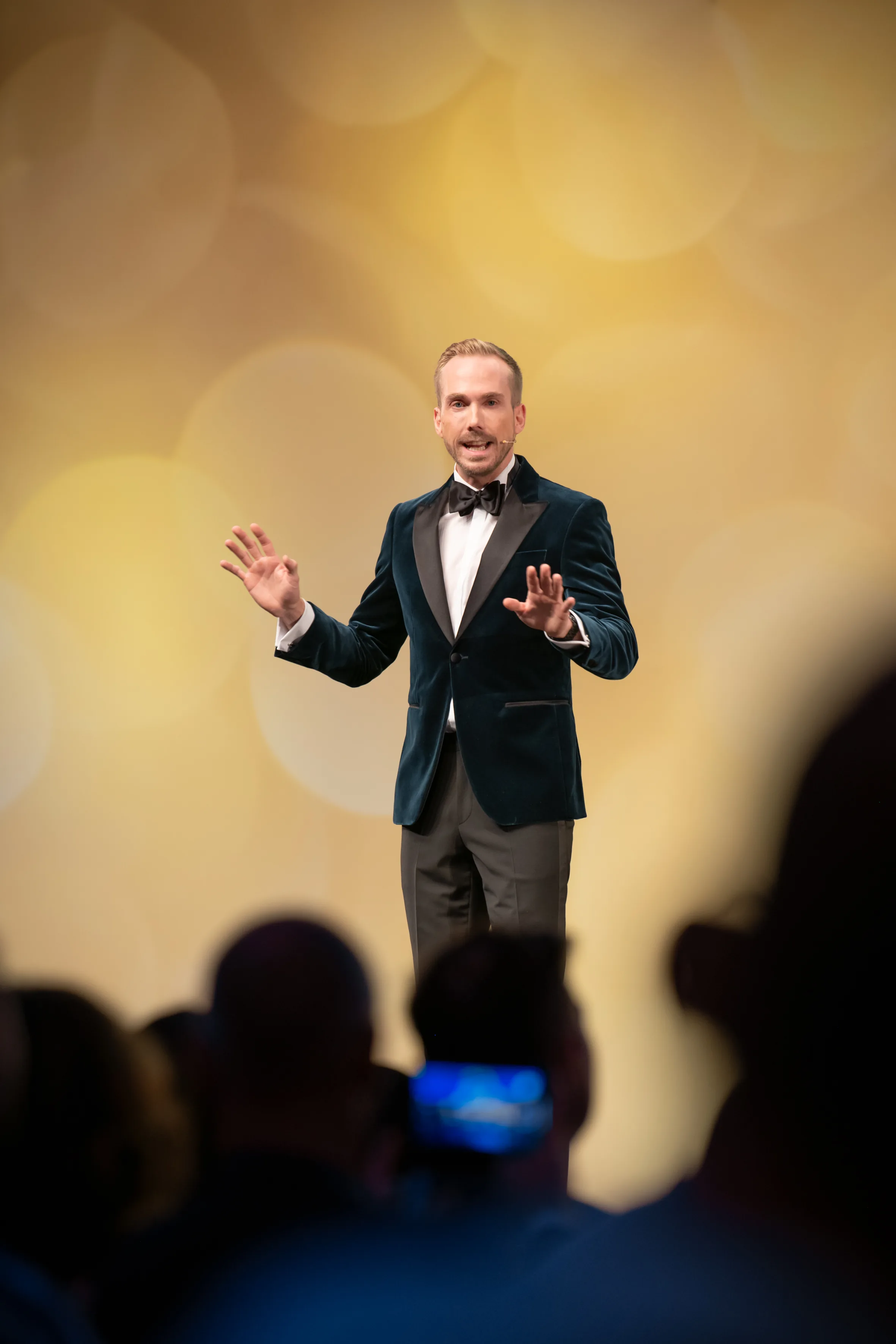 Felix Uhlig in ganzer Figur vor der goldenen Bühnenwand der Meister- und Meisterinnenfeier der Handwerkskammer Hannover 2023