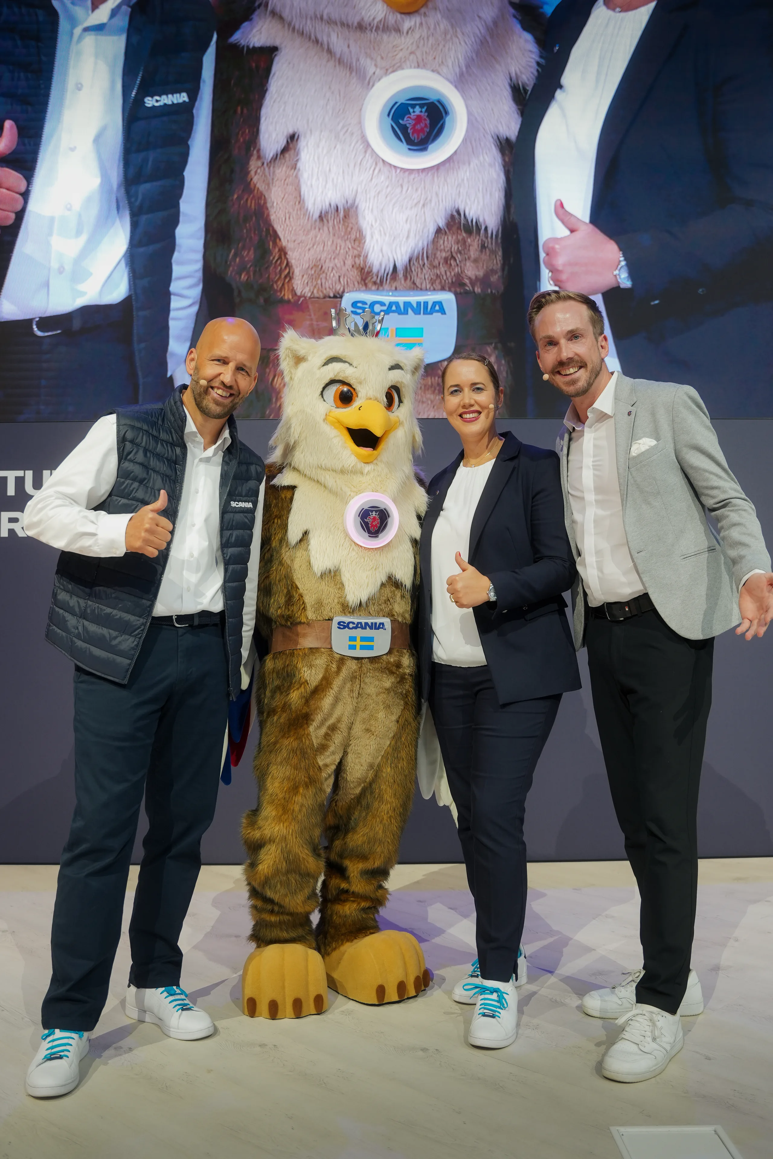Felix Uhlig mit dem Scania-Maskottchen und zwei Gästen auf der Messebühne in Hannover