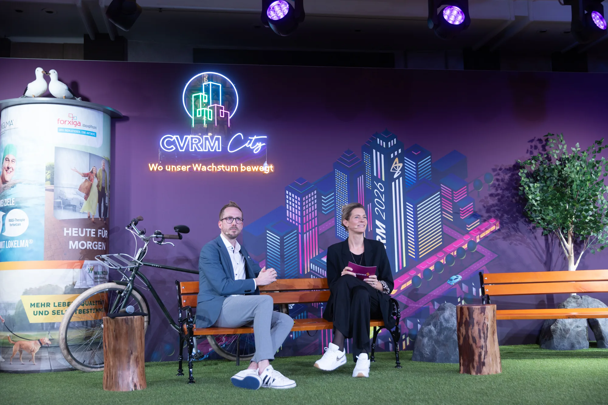 Gespräch auf der Bühne der AstraZeneca CVRM Tagung 2026 in Berlin vor dem Bühnenbild CVRM City