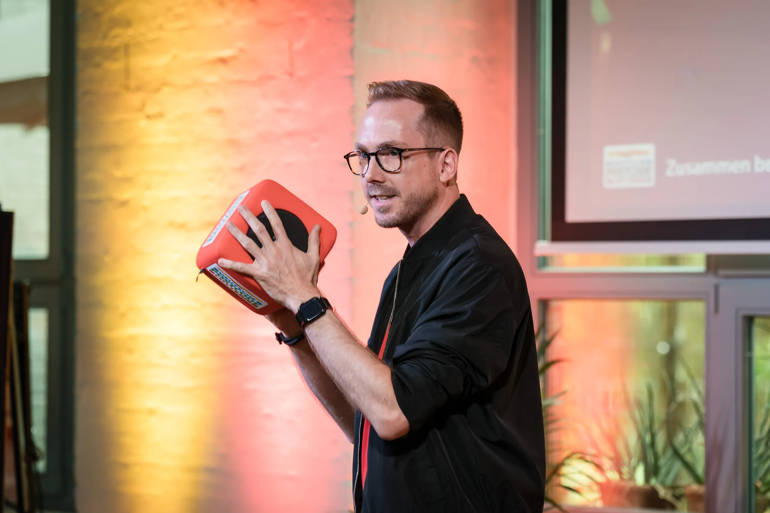 Felix Uhlig hält eine Karte hoch beim Partnertreffen der Deutschen Postcode Lotterie 2025