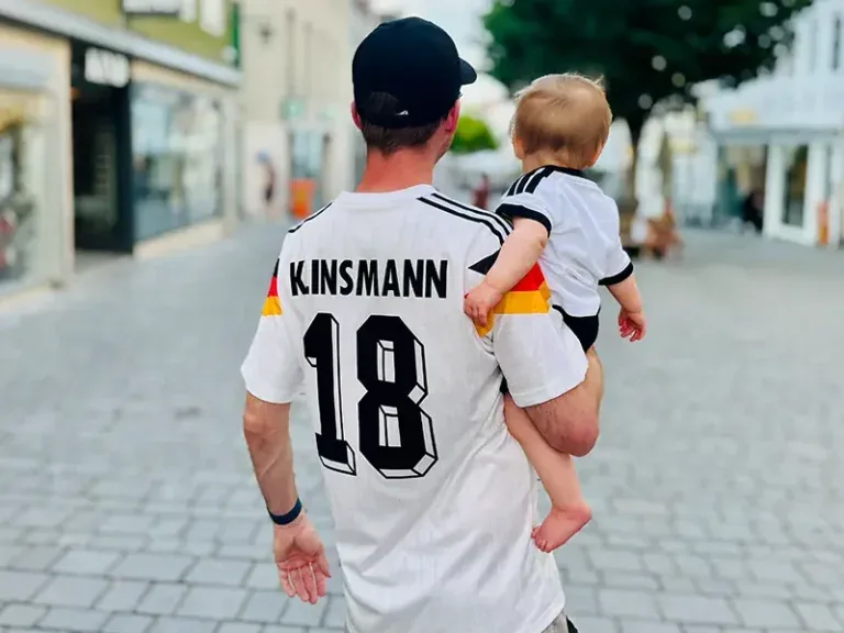 Felix Uhlig privat, von hinten, mit seinem Kind auf dem Arm im Fußballtrikot